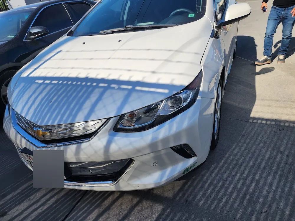 Front view of a white Chevrolet Volt's bumper and hood in a body shop lot