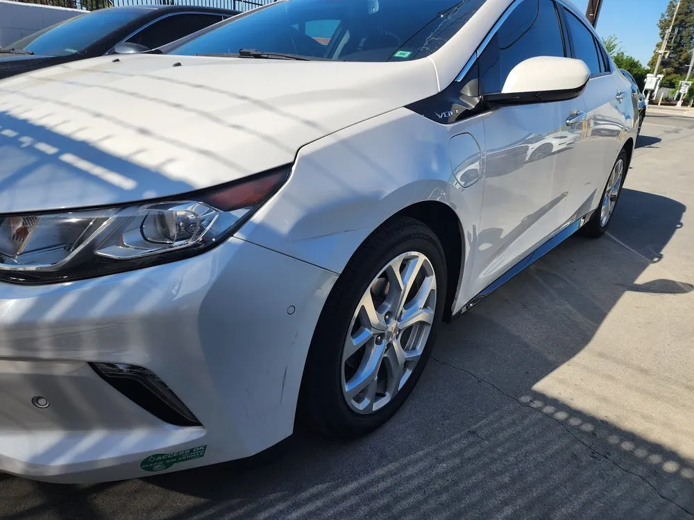 White Chevrolet Volt's front bumper and fender with scuffs, parked for body repair