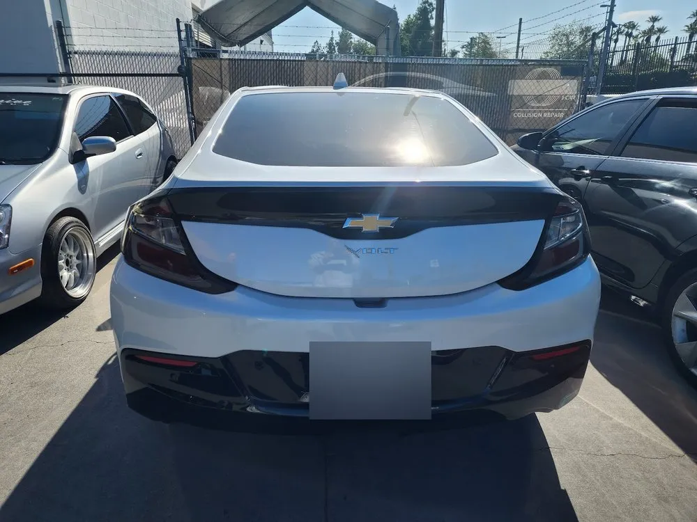Rear view of a white Chevrolet Volt hatchback parked in a fenced collision repair lot