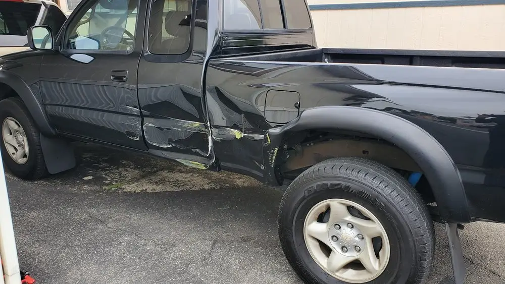 Black pickup truck with crushed doors and a dented bed side before collision repair